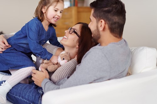 A close up of a family of three hugging in a white sofa in their livingroom.
