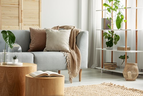 An interior from a livingroom with a sofa, table, shelf, plant etc in grey, beige, brown and green colors.
