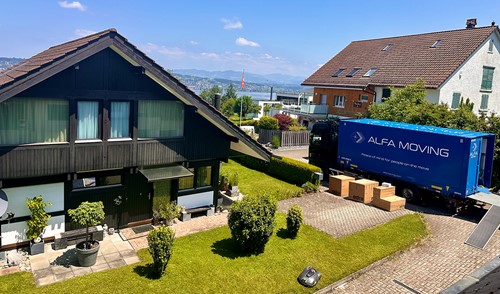 An Alfa Moving truck by a house unloading Alfa Moving boxes for a move.