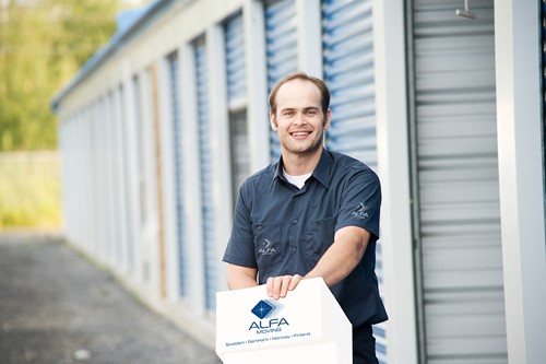 An Alfa Moving crew person with a white box with Alfa Moving logo outside a warehouse setting.